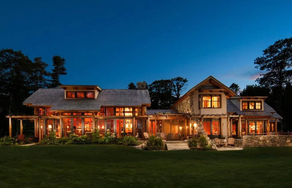 Timber and stone home glowing at dusk with a wide lawn in front