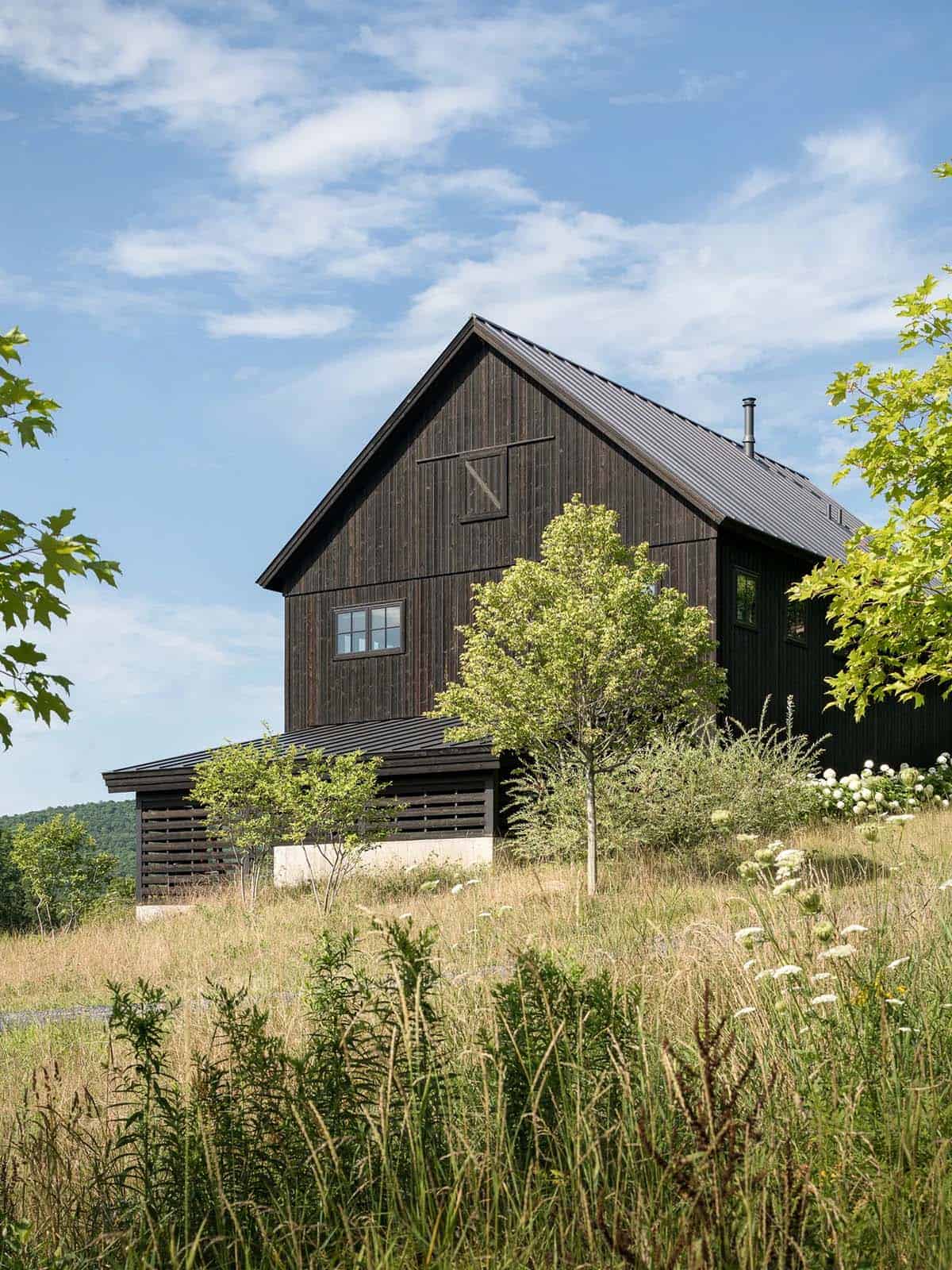 Black barn-style house exterior surrounded by wildflower meadow