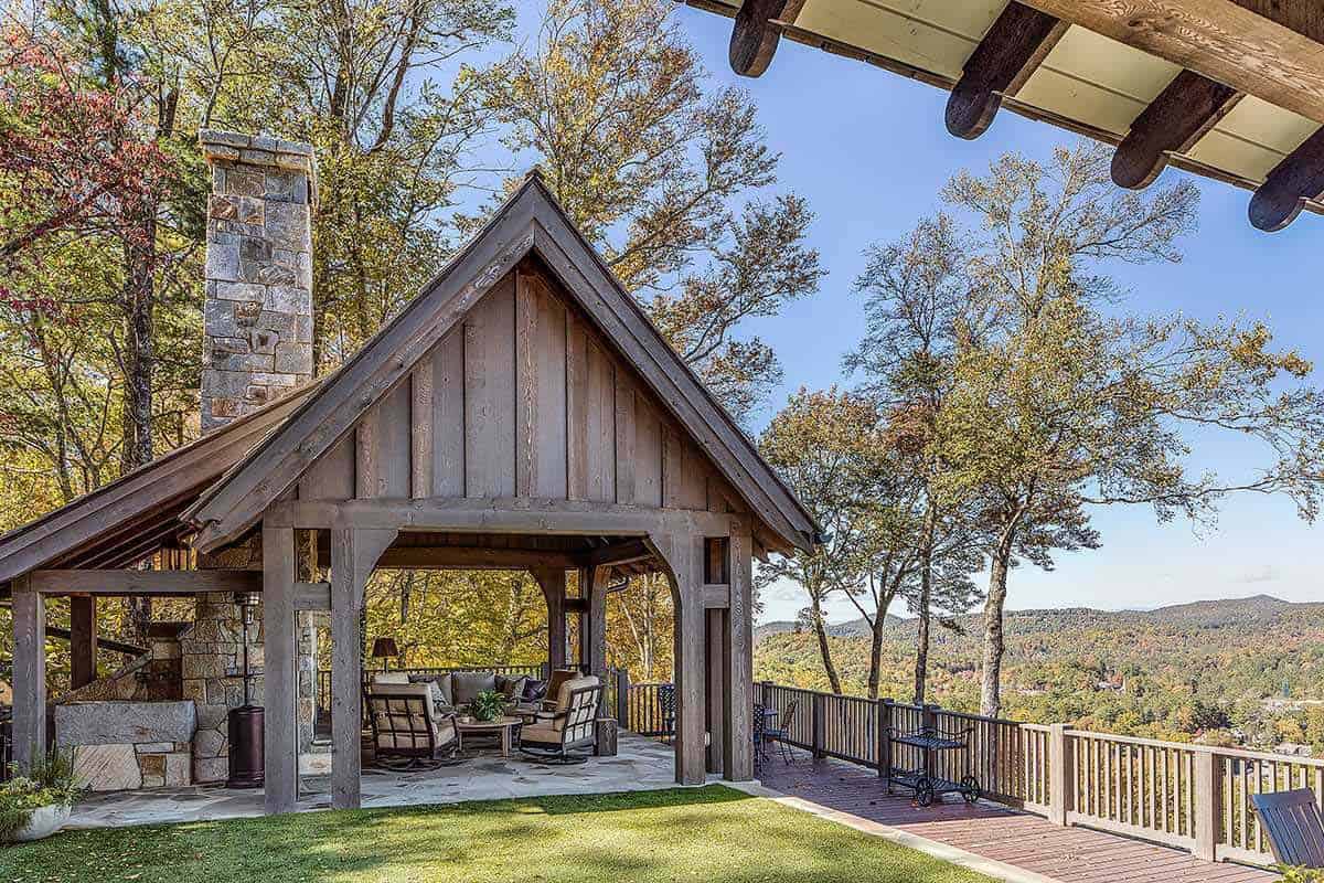Rustic timber pavilion with stone chimney overlooking layered mountain ridges