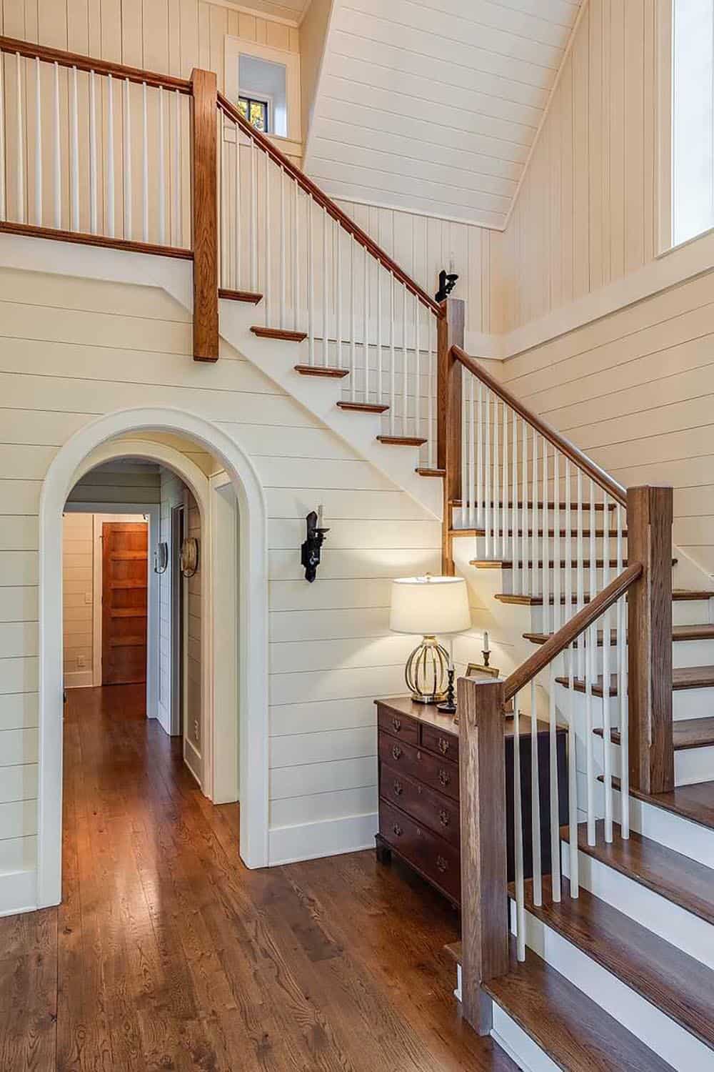 Curved staircase with shiplap walls and arched hallway passage below