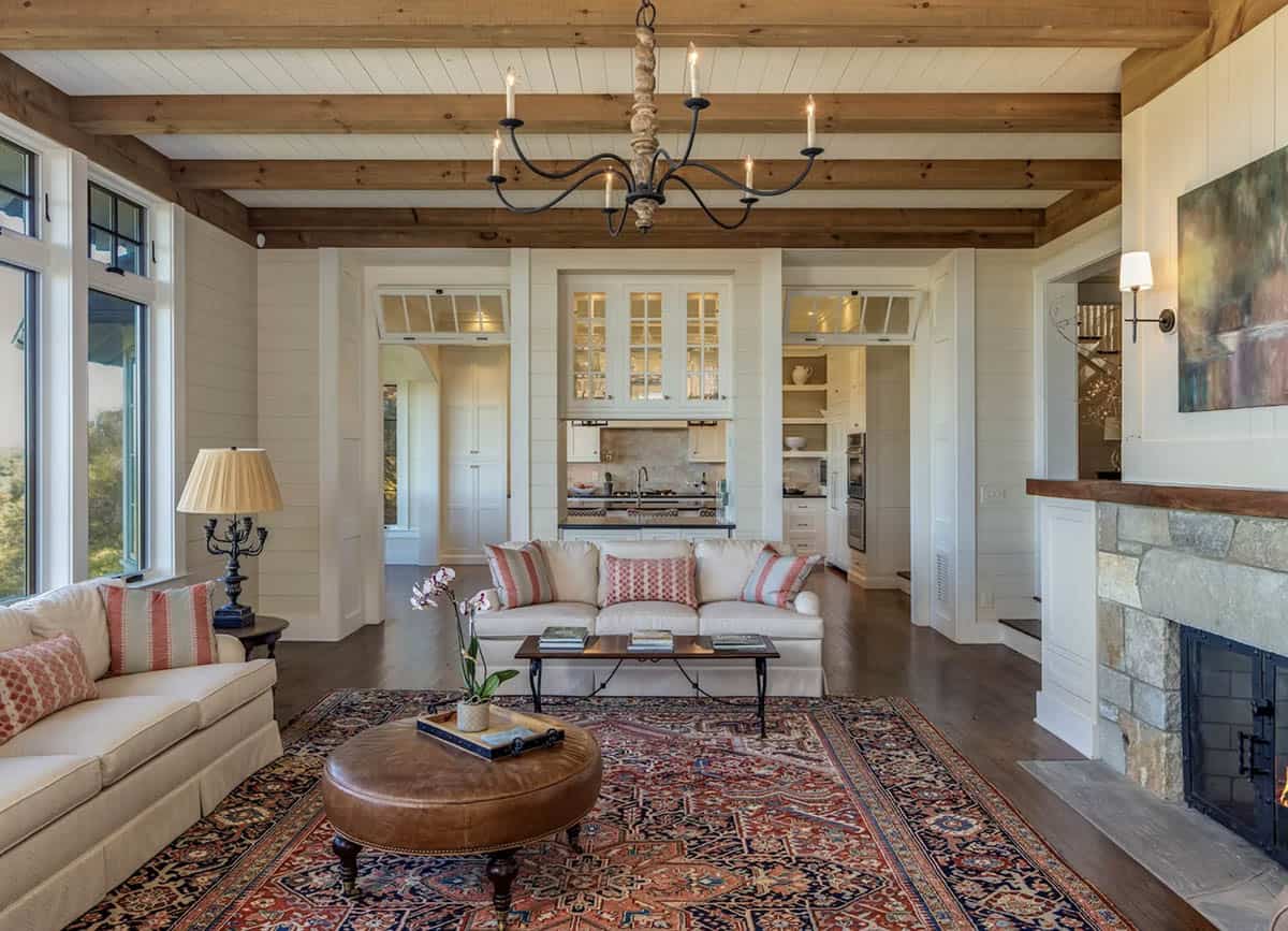 Beamed living room with stone fireplace opens to kitchen beyond