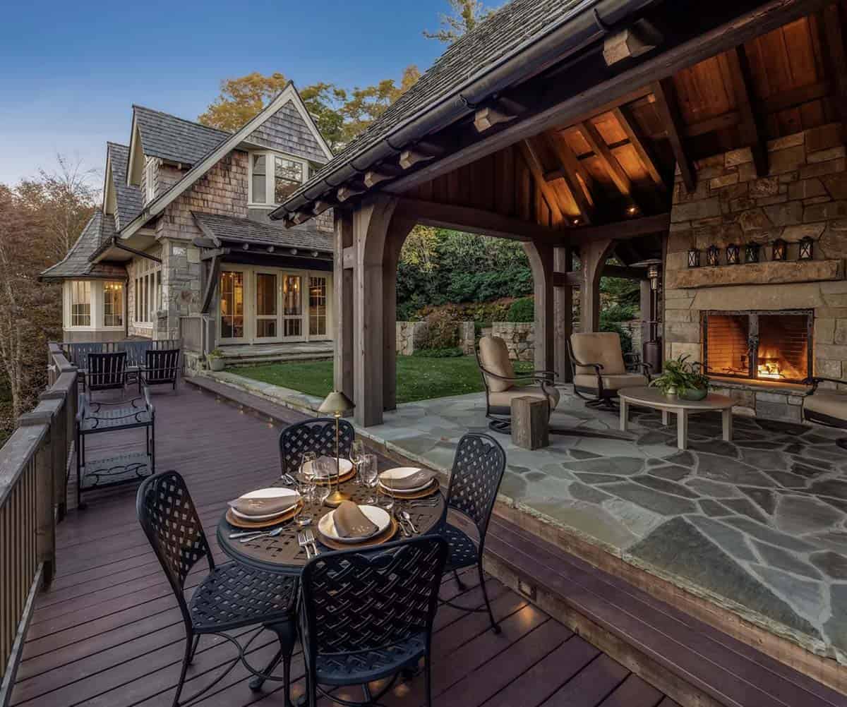 Outdoor dining table beside stone fireplace on covered evening deck
