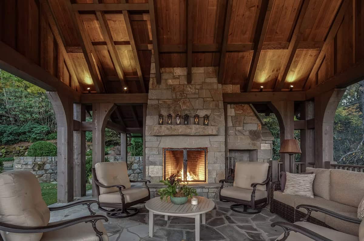 Covered stone patio with glowing fireplace and wraparound seating area
