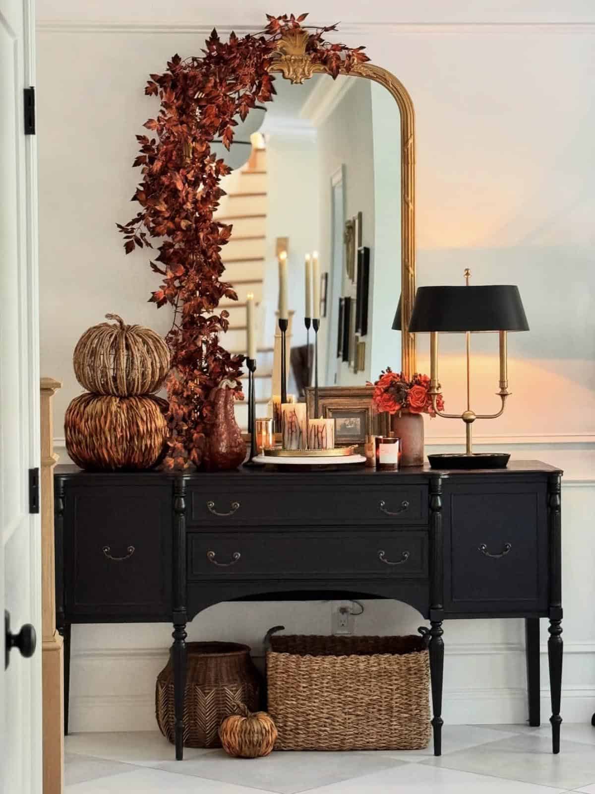 Gold mirror draped with a brown seeded garland over a black console