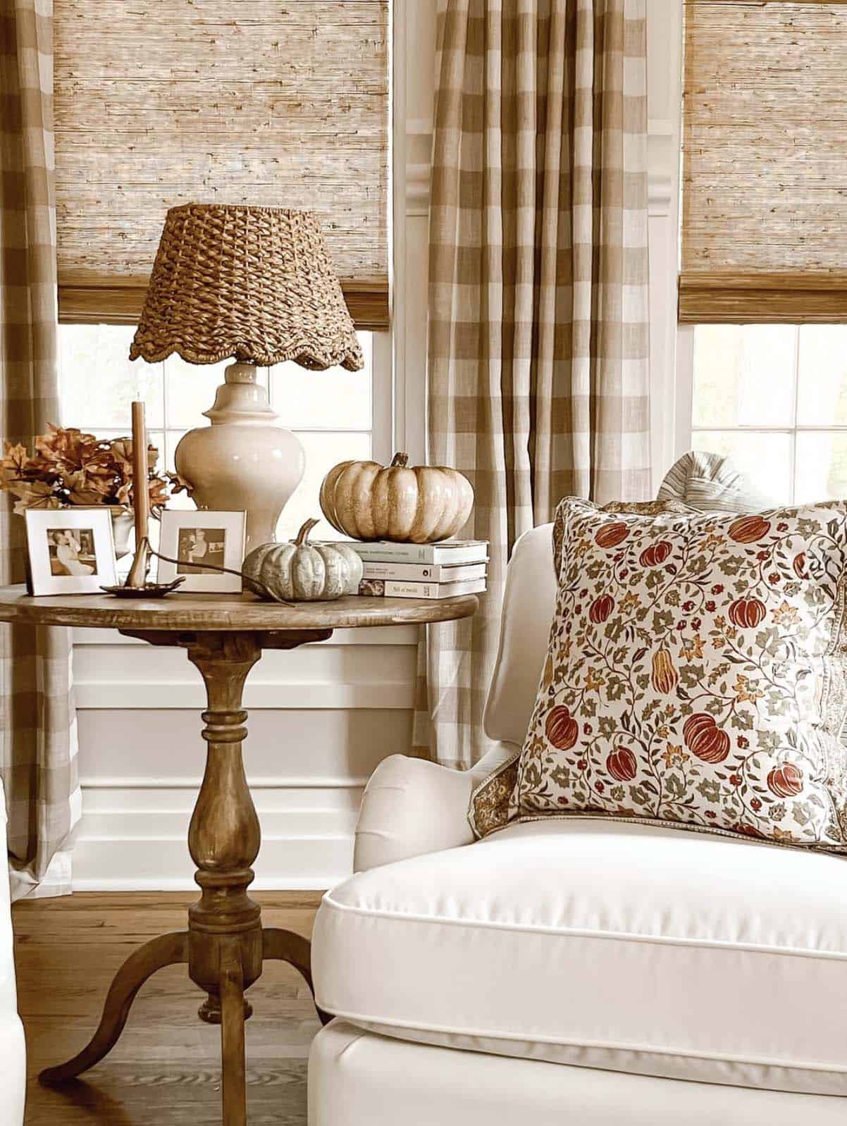 Round wood side table with pumpkins, lamp, and floral pillow chair in corner