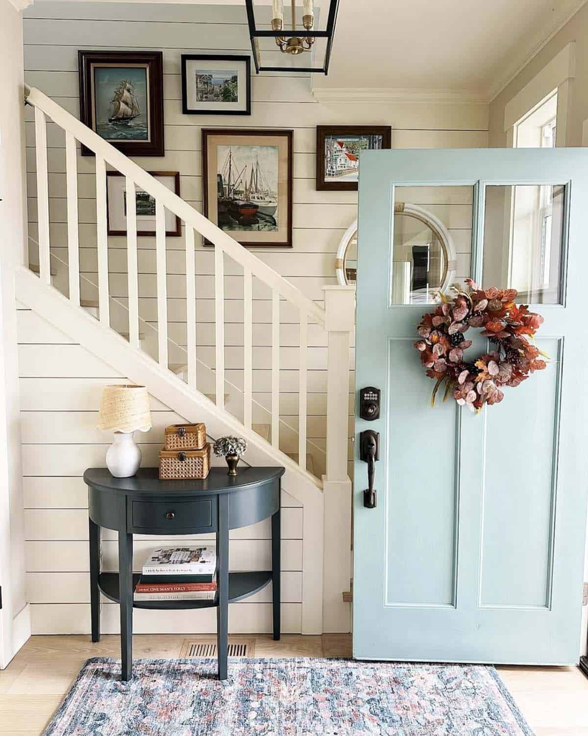 Half-round entryway table in front of a staircase beside an open door with a fall wreath