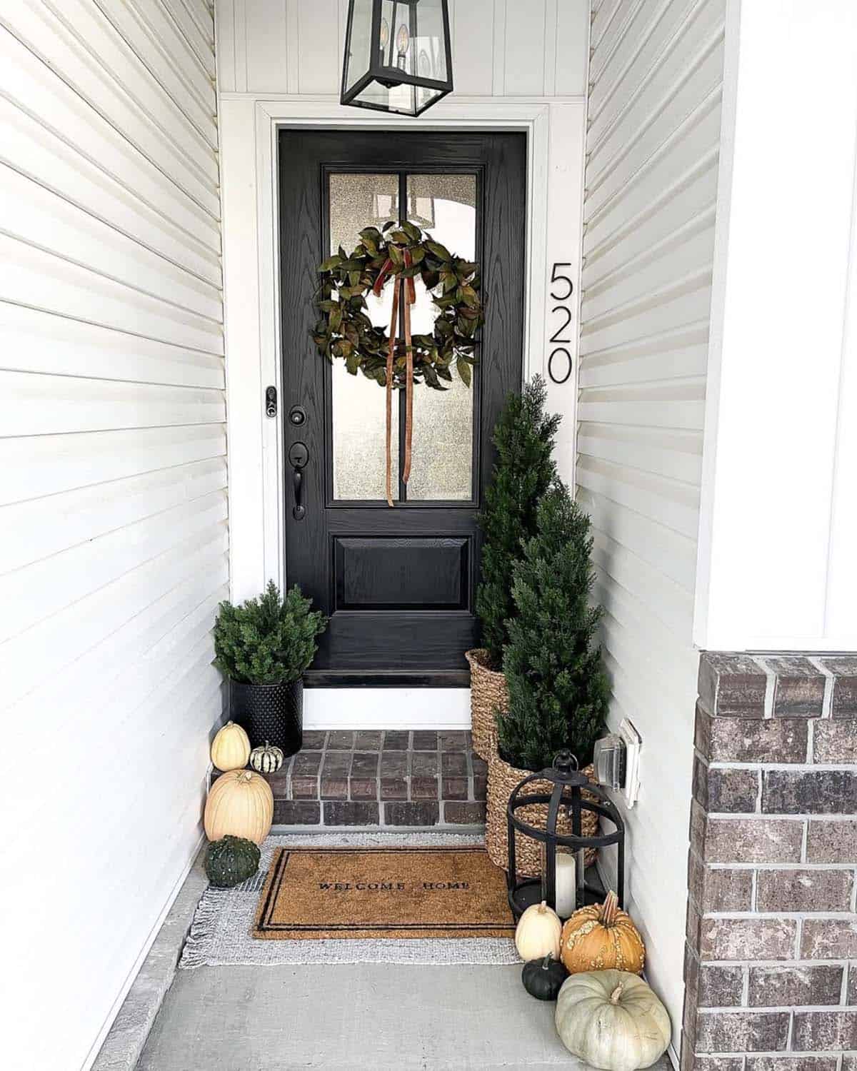 Small fall entryway with black door, faux cedar trees, wreath, and pumpkins