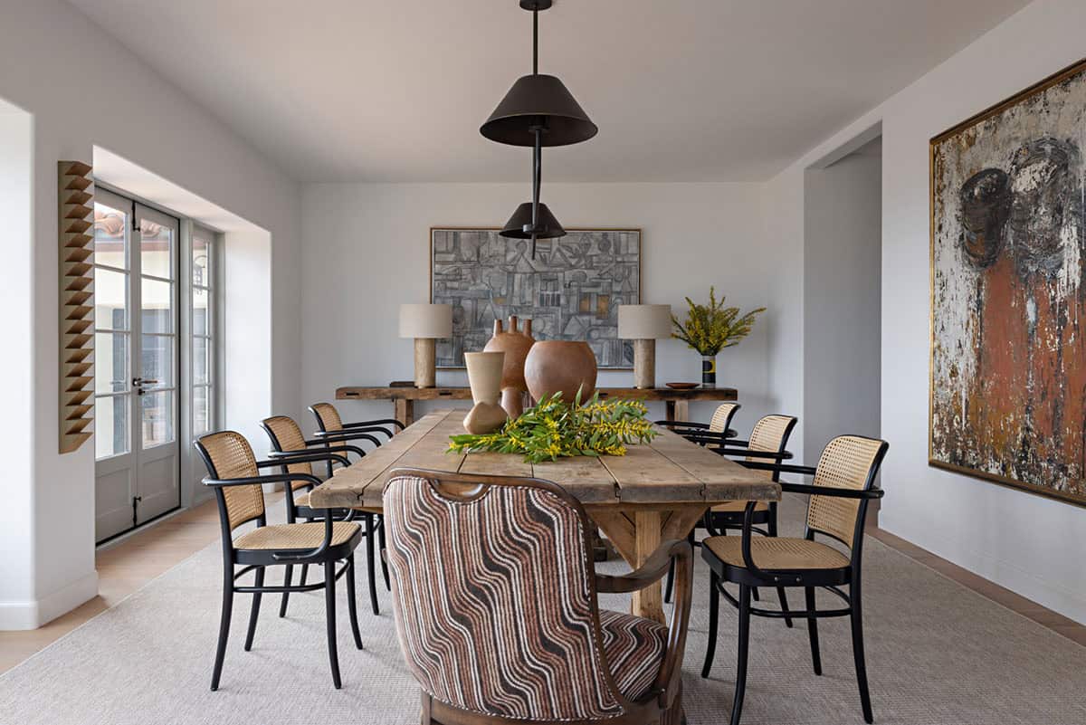 Dining room with rustic wood table, cane chairs, and large abstract artwork