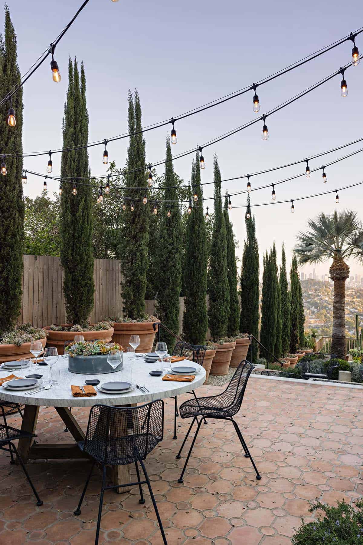 Outdoor dining patio with marble table, string lights, and potted cypress trees