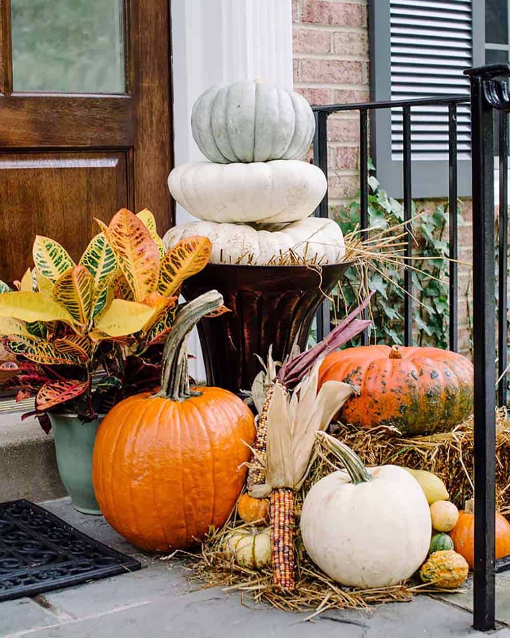 Stacked white pumpkins in an urn beside Indian corn and hay bale