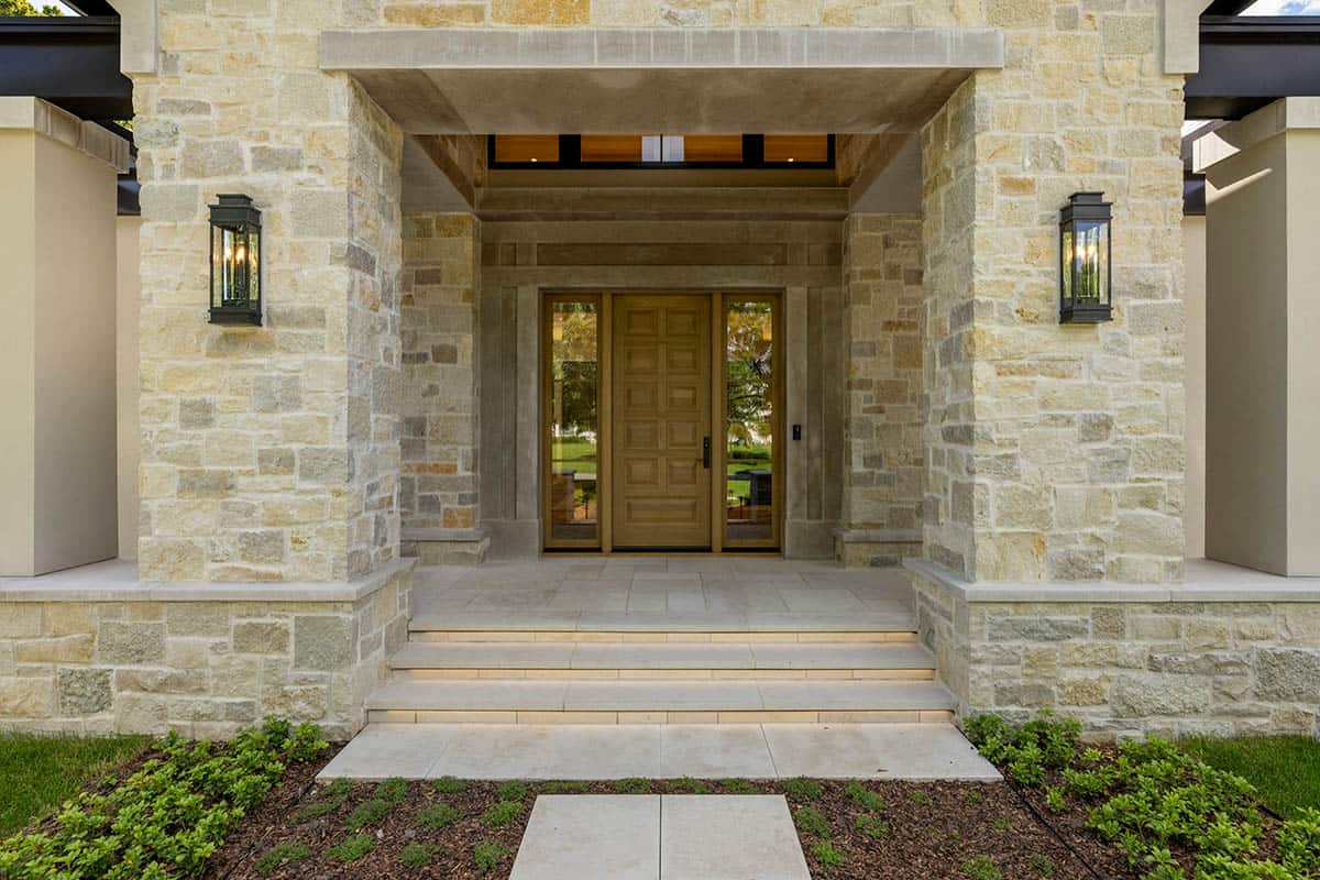 Covered stone entryway with wood door and stacked step lighting