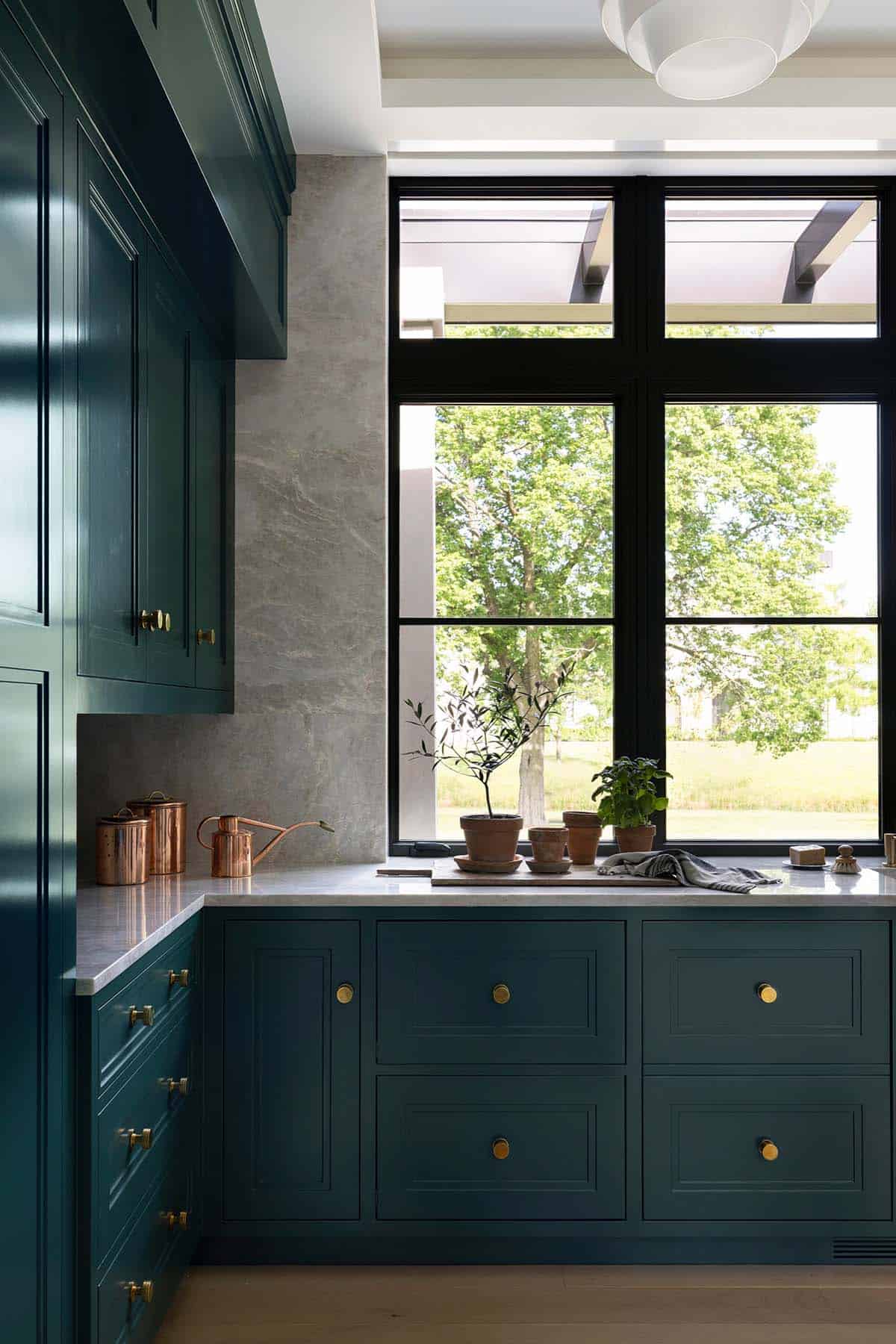 Dark teal cabinetry with brass hardware beside black-framed window