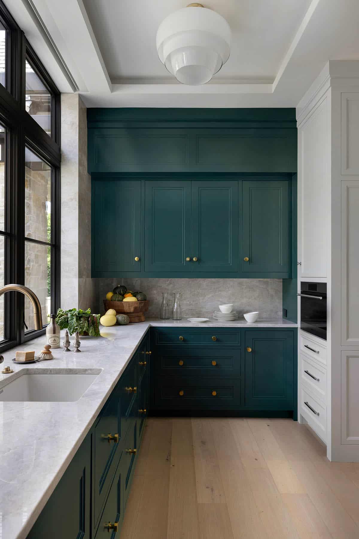 Teal cabinetry with brass pulls flanking built-in wall oven