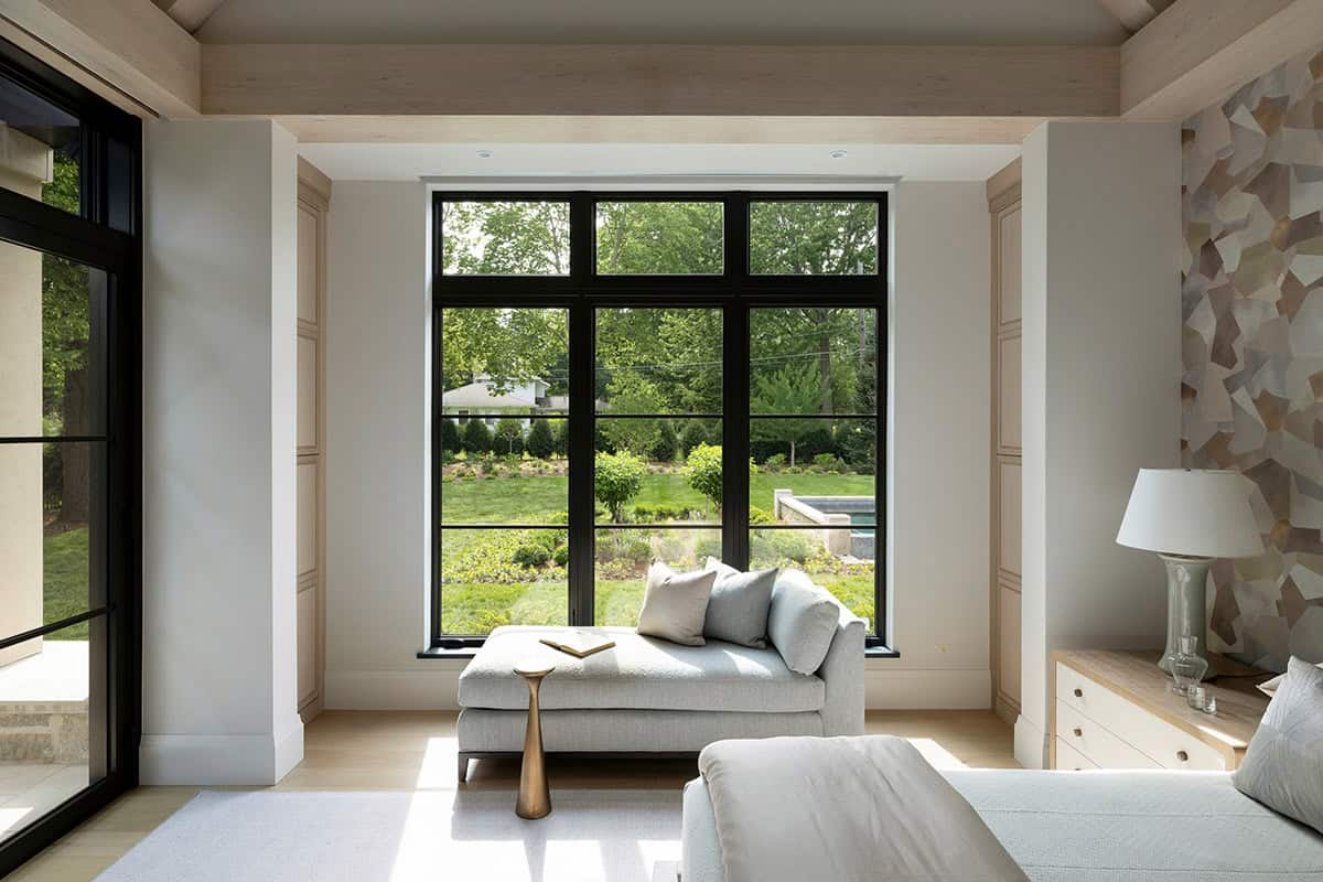 Bedroom chaise lounge framed by tall black steel windows