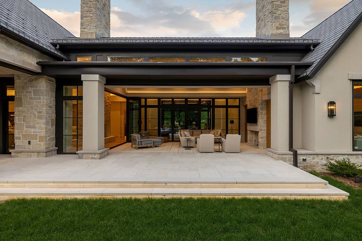 Covered patio with stone chimney opening to lit living room
