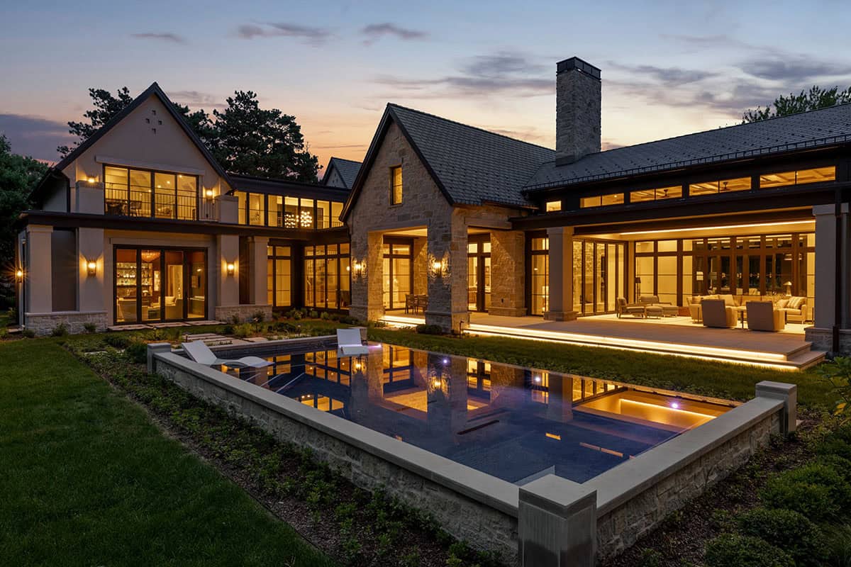 Aerial-angle rear view of home with illuminated pool at dusk