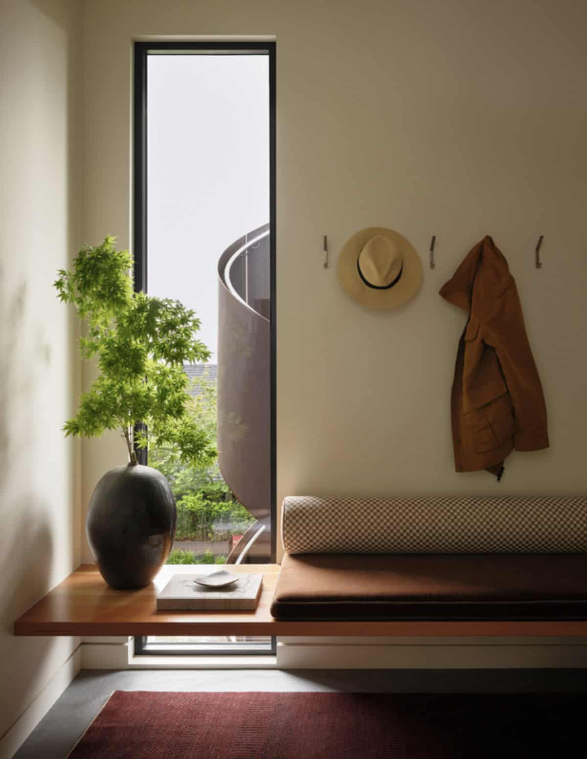 Entry bench with woven cushion beneath a narrow window view of the stair