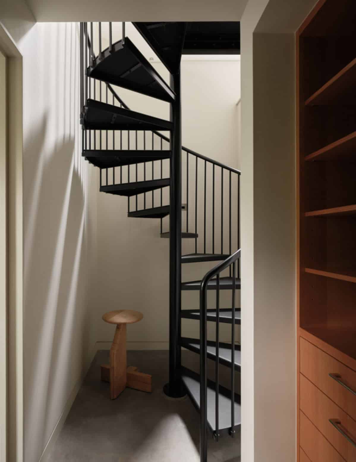 Black spiral staircase with round wood stool inside closet nook