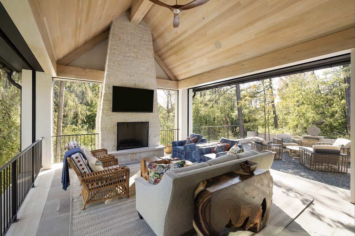 Covered porch with stone fireplace and wicker seating overlooking woods