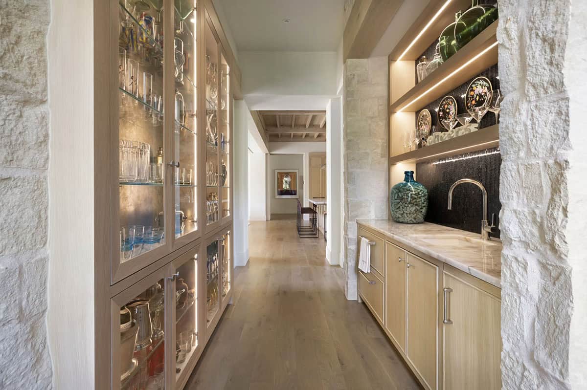 Butler's pantry hallway with lit glass cabinetry and stone archway