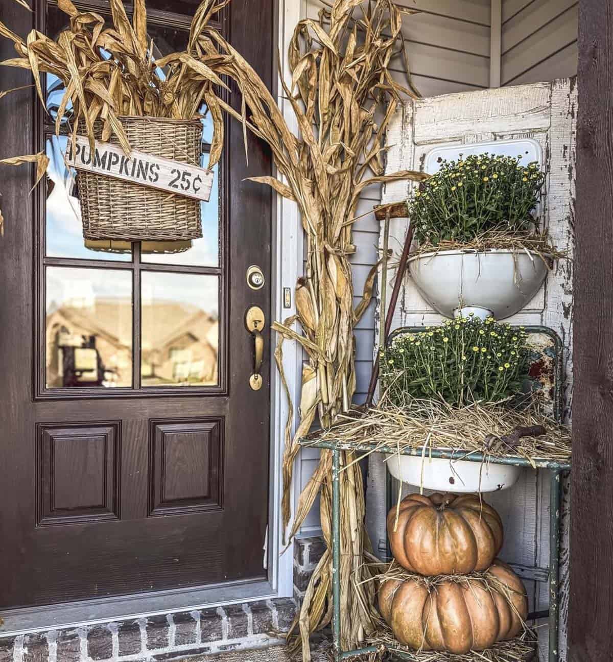 Porch corner with vintage door, enamel basins, mums, pumpkins, and corn stalks