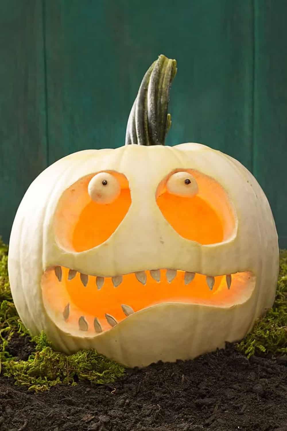 White jack-o’-lantern with pumpkin seed teeth and round eyeballs perched in its carved eye openings