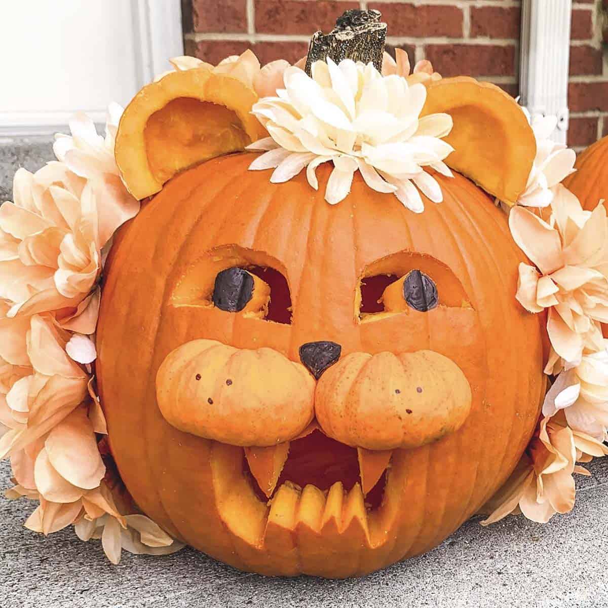 Lion jack-o’-lantern with a faux flower mane, pumpkin ears, a mini pumpkin muzzle, and carved fangs