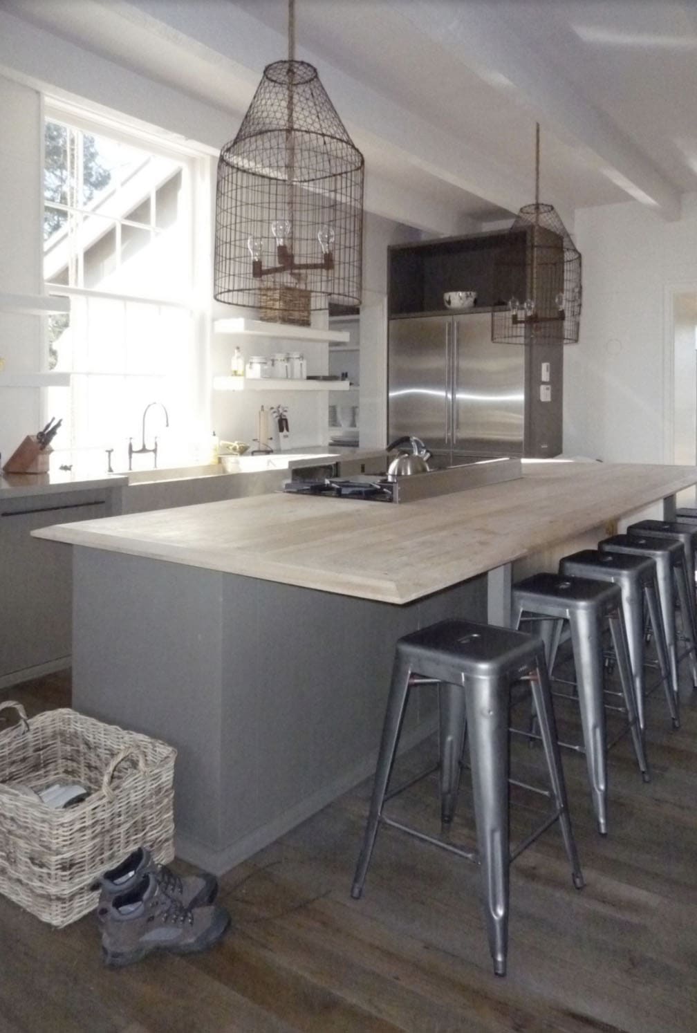 Kitchen island with a whitewashed wood top, metal stools, and wire catfish-trap pendant lights