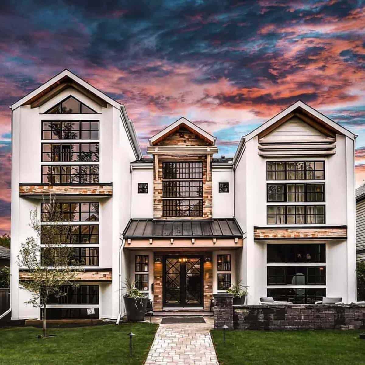 Modern farmhouse exterior in Calgary at sunset, with white gables, black-framed windows, and reclaimed wood accents