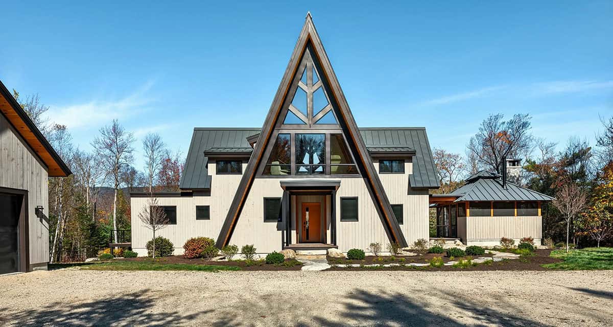 Front view of an A-frame home with a triangular glass gable, dark metal roofs, a covered entry and a screened porch beside it