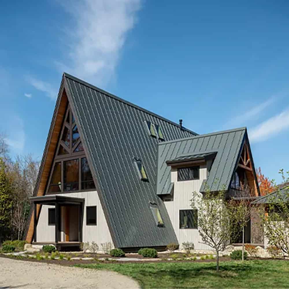 A-frame home with a steep green-gray metal roof, roof skylights, a covered entry and a smaller gabled wing beside it