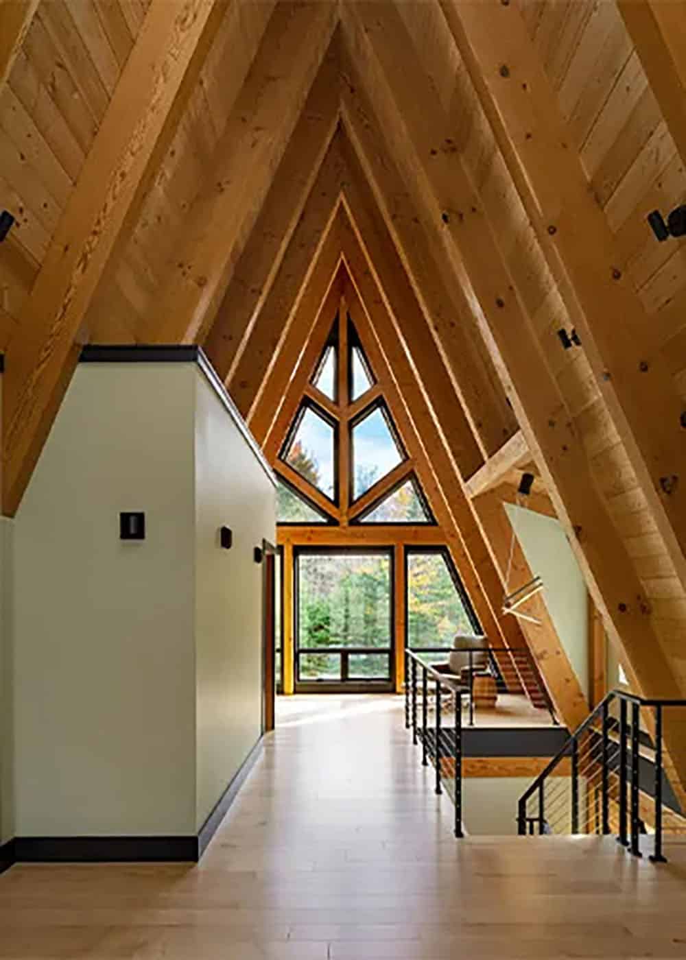 Upstairs hallway under steep A-frame rafters leading to a triangular window with timber mullions