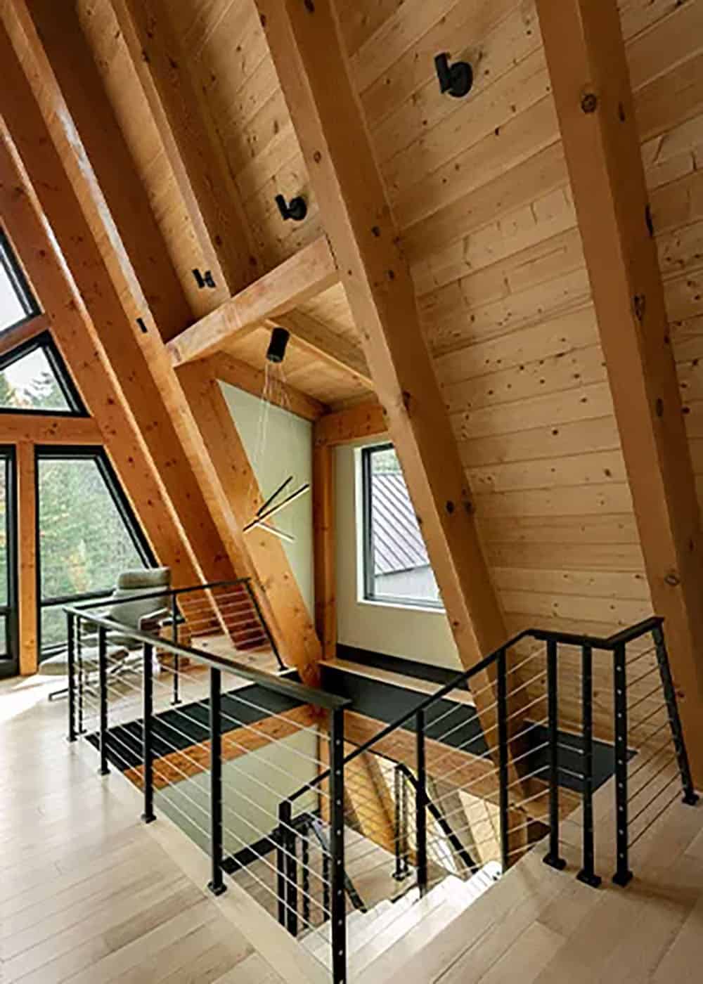 Upper landing with black cable railings, sloped wood ceilings, timber rafters and a linear pendant above the stairs