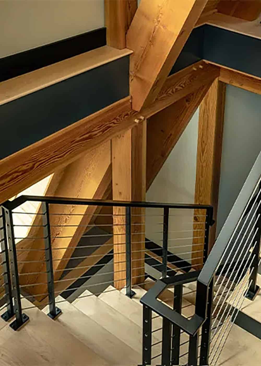 Staircase with light wood treads and black cable railings beside timber posts and diagonal braces
