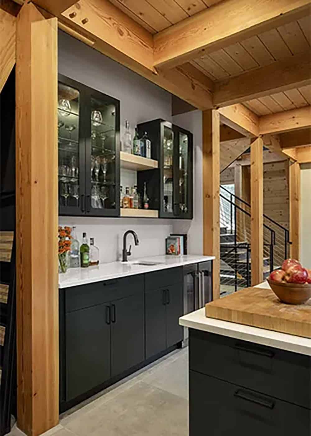 Bar with black cabinets, glass-front upper cabinets with glassware and a black faucet, framed by timber posts