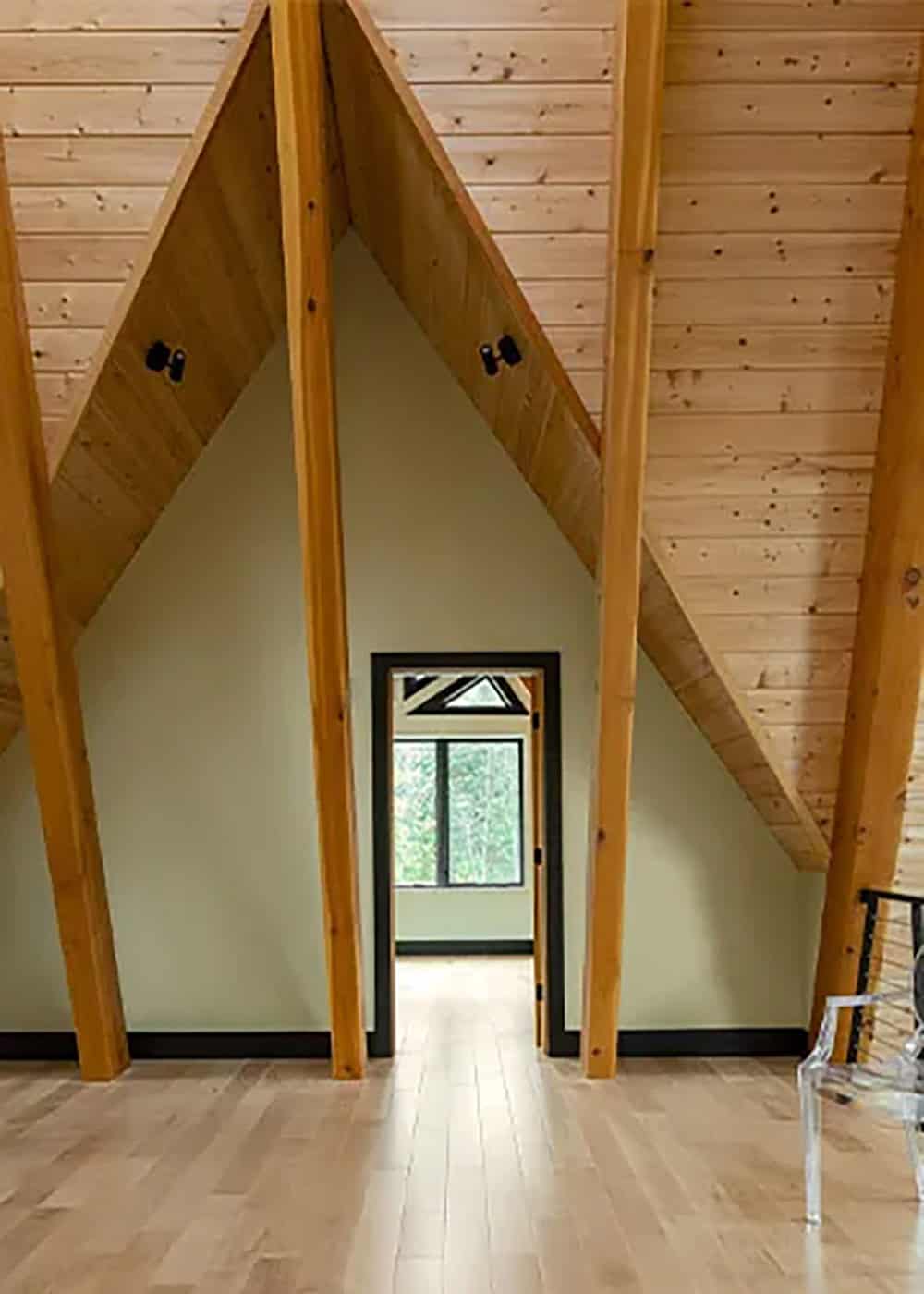 Loft wall with sloped wood ceiling planes and two diagonal timber braces flanking a black-framed doorway to a bedroom