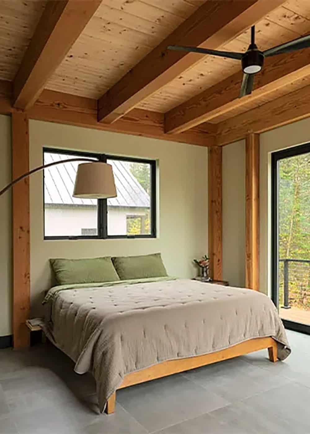 Bedroom with a timber-beamed wood ceiling, taupe bedding, an arc floor lamp and a glass door to a balcony