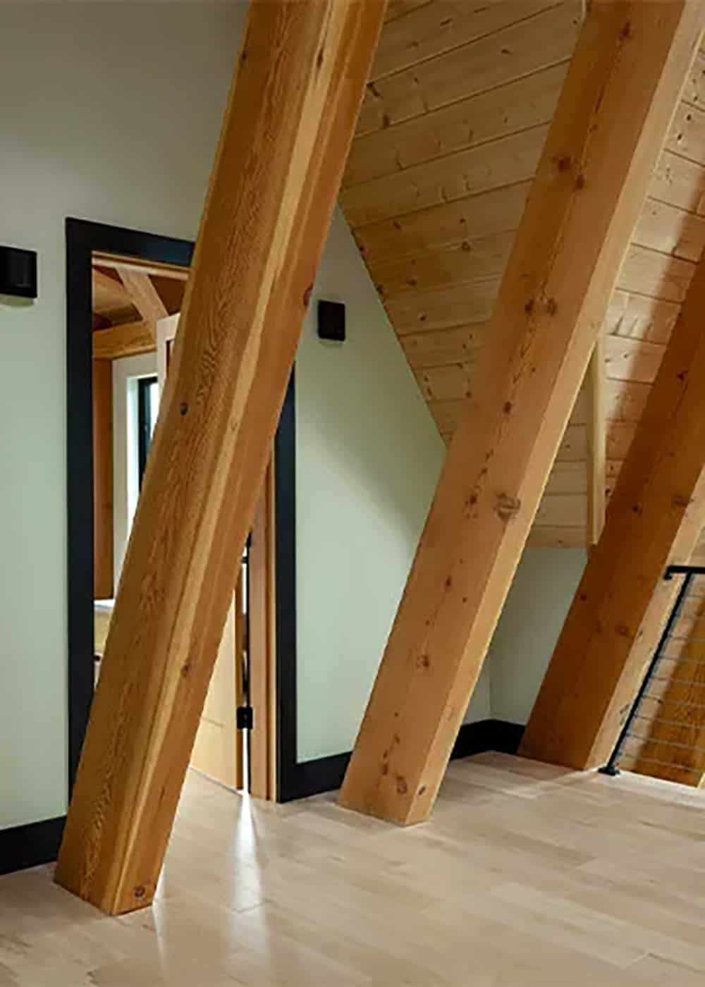 Upstairs hallway with two angled timber rafters rising from the wood floor to a sloped plank ceiling