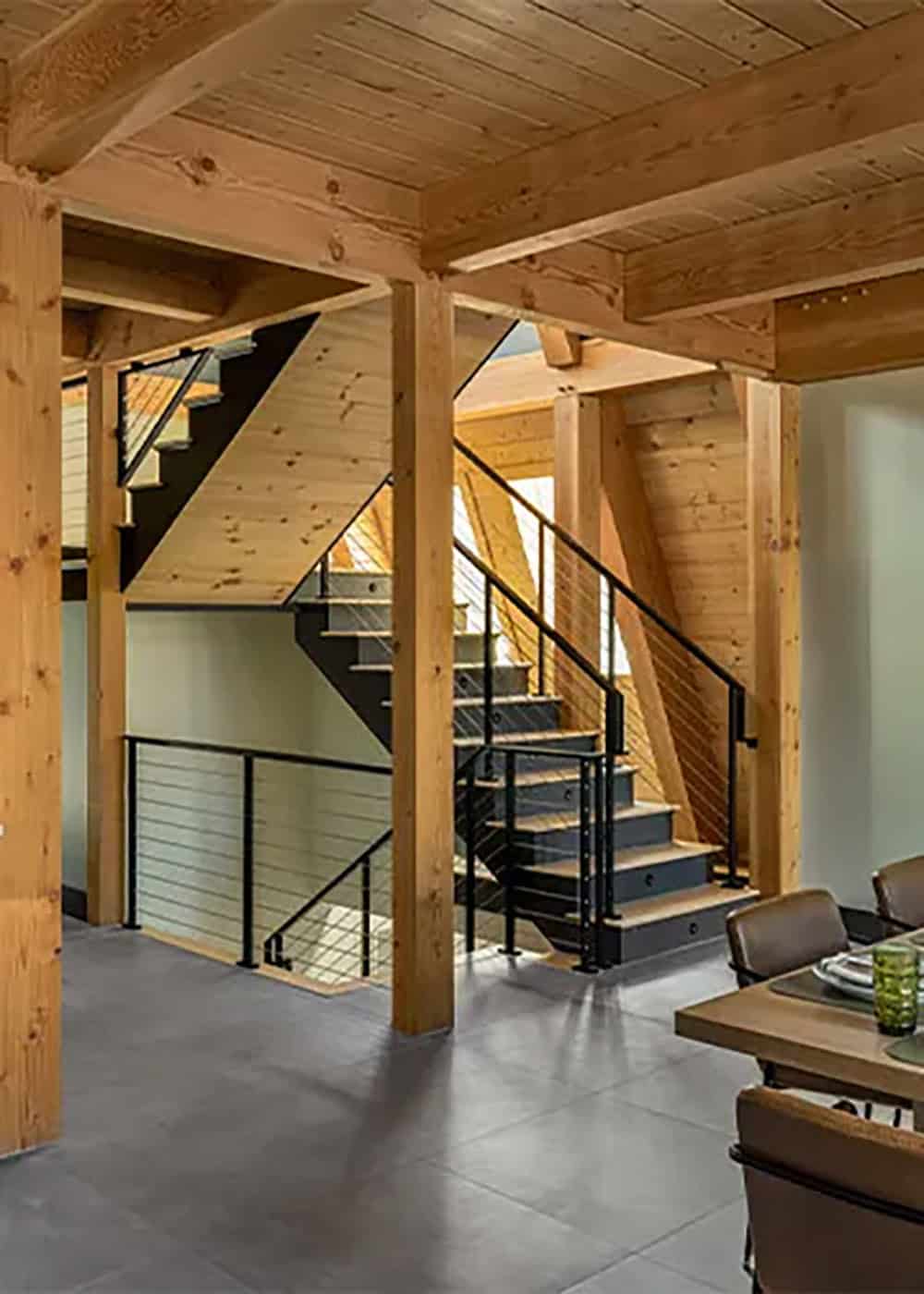 Staircase with black steel stringers and cable railings rising between timber posts beside the dining area