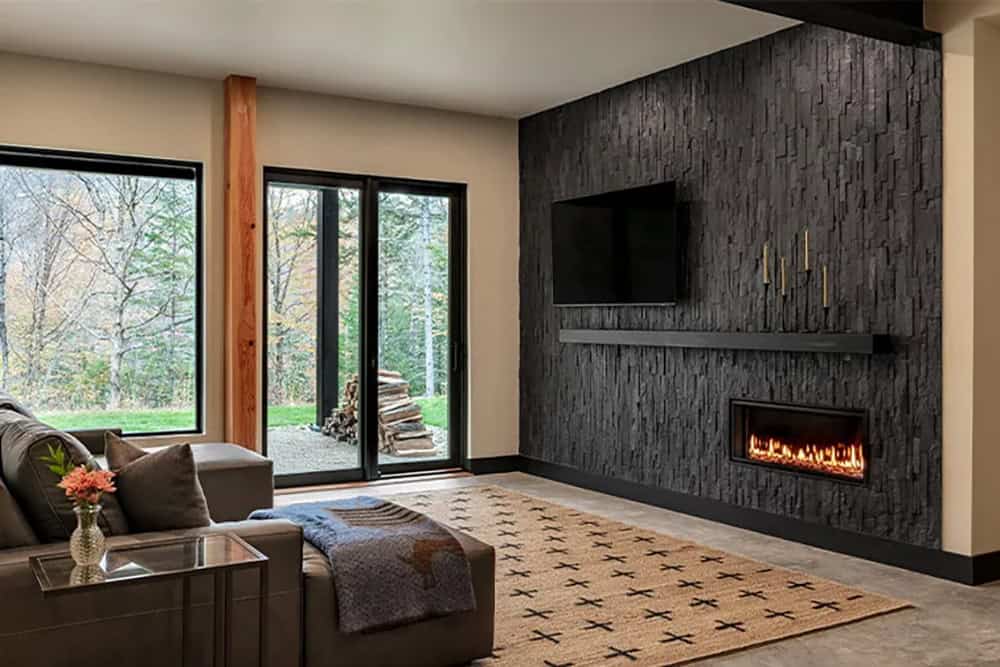 Lower-level family room with a black stacked stone wall, a linear gas fireplace, a TV and sliding doors to the yard