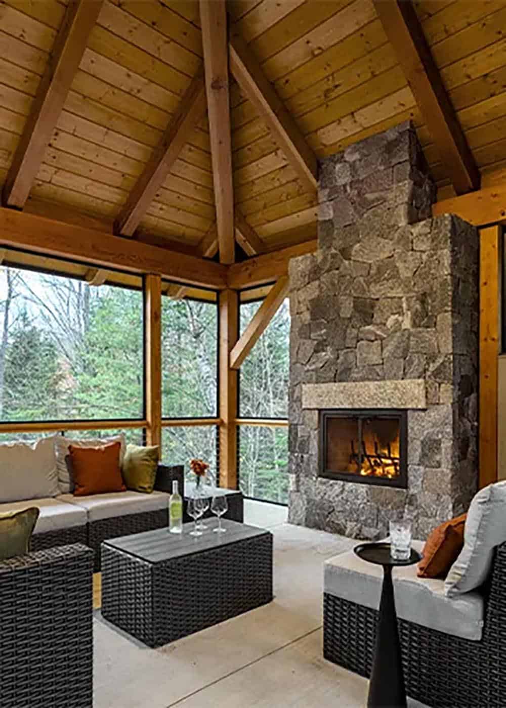 Screened porch with a wood-burning fireplace in a stone chimney, wicker seating and a vaulted timber ceiling