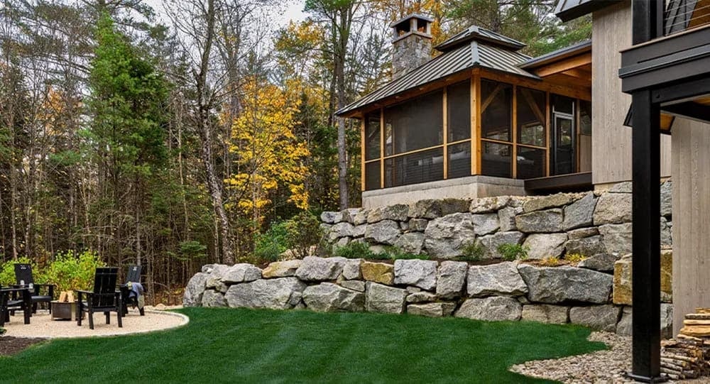 Backyard lawn below tiered boulder retaining walls, with a fire pit patio and the screened porch above