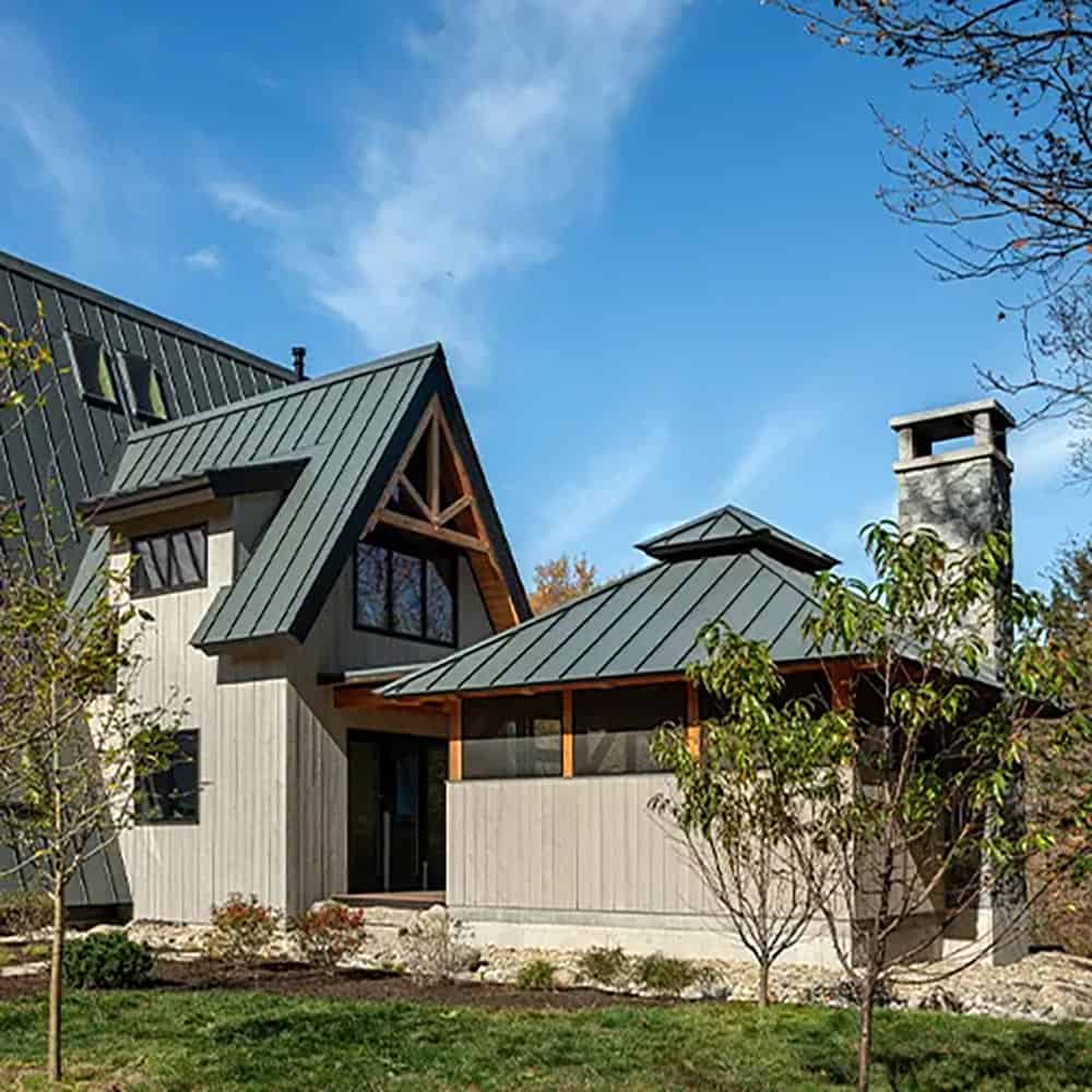 Side of the home with a timber-trussed gable, metal roofs and the screened porch with its tall stone chimney