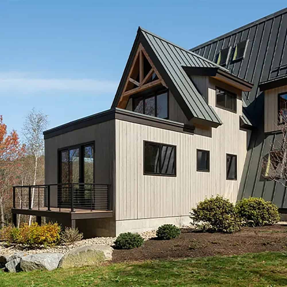 Gabled wing with an exposed timber truss, vertical wood siding and a small deck with black horizontal railing
