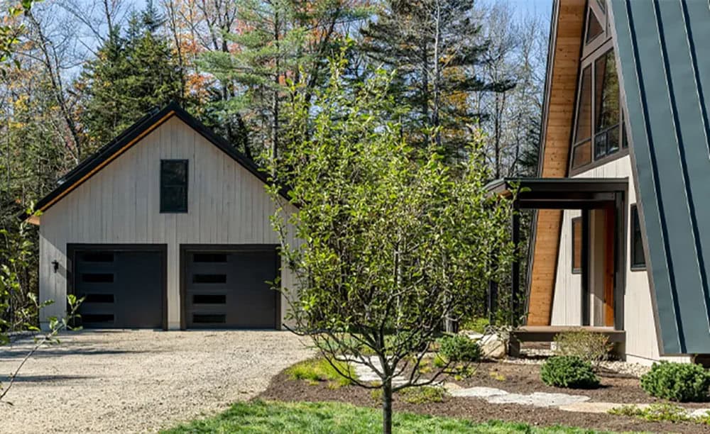 Detached two-car garage with black windowed doors beside the covered front entry of the A-frame home