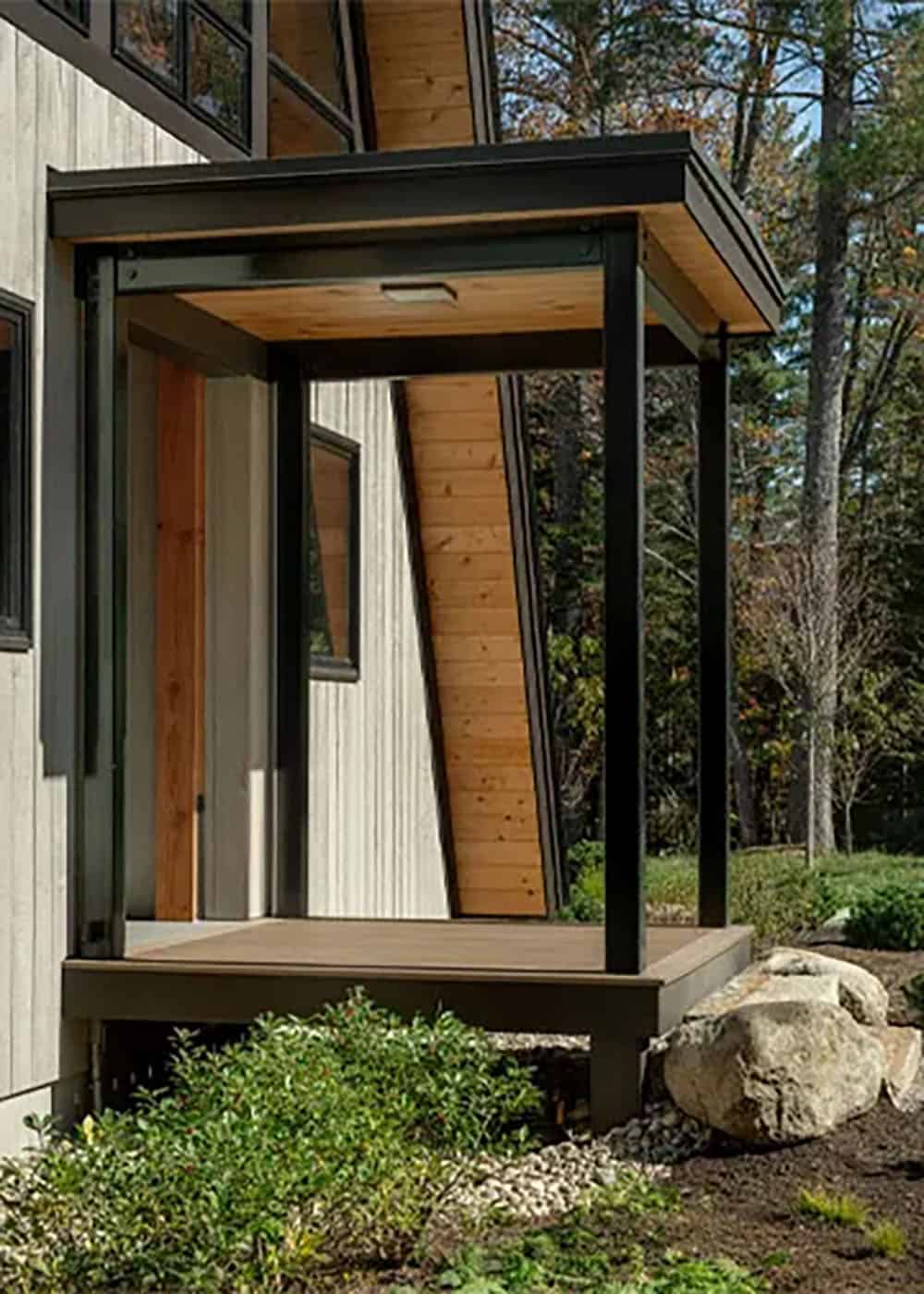 Covered entry porch with a black steel frame, a wood soffit and a composite deck beside the angled A-frame wall