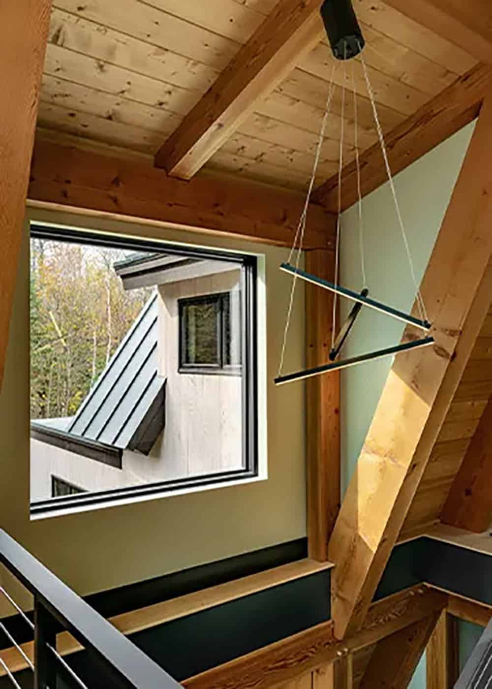 Stair landing with a large black-framed window looking out to a metal roof, beside a suspended linear pendant