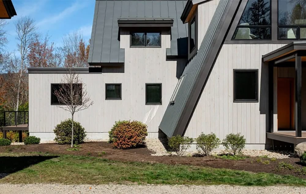 Front facade with vertical wood siding, black windows, a dormer and the sloping A-frame roof beside the entry porch