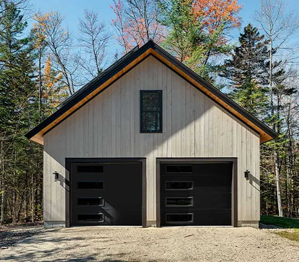 Detached two-car garage with vertical wood siding, black doors with glass panels and a wood soffit