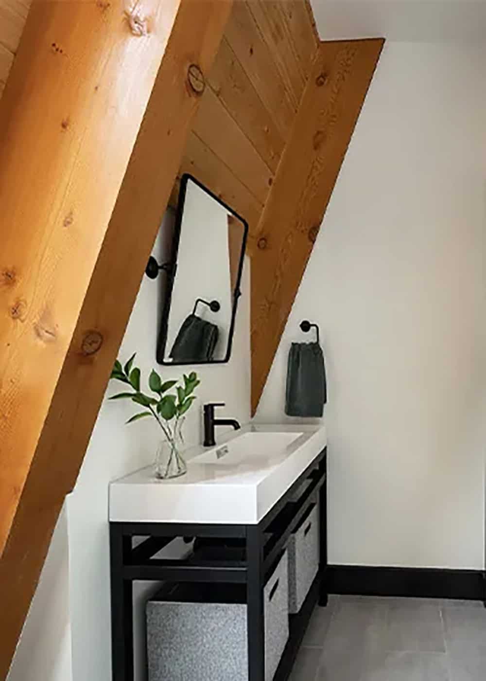 Bathroom with a white sink on a black metal vanity and a pivoting mirror set below a sloped timber rafter
